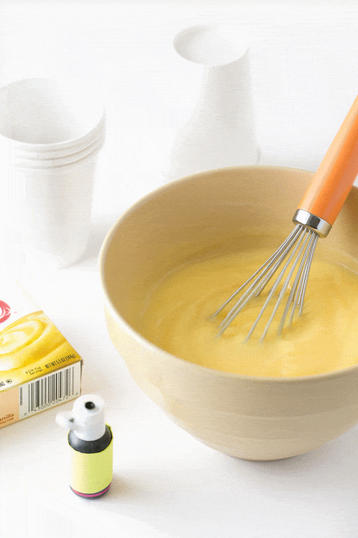 Mixing green food coloring into bowl of vanilla pudding with whisk.