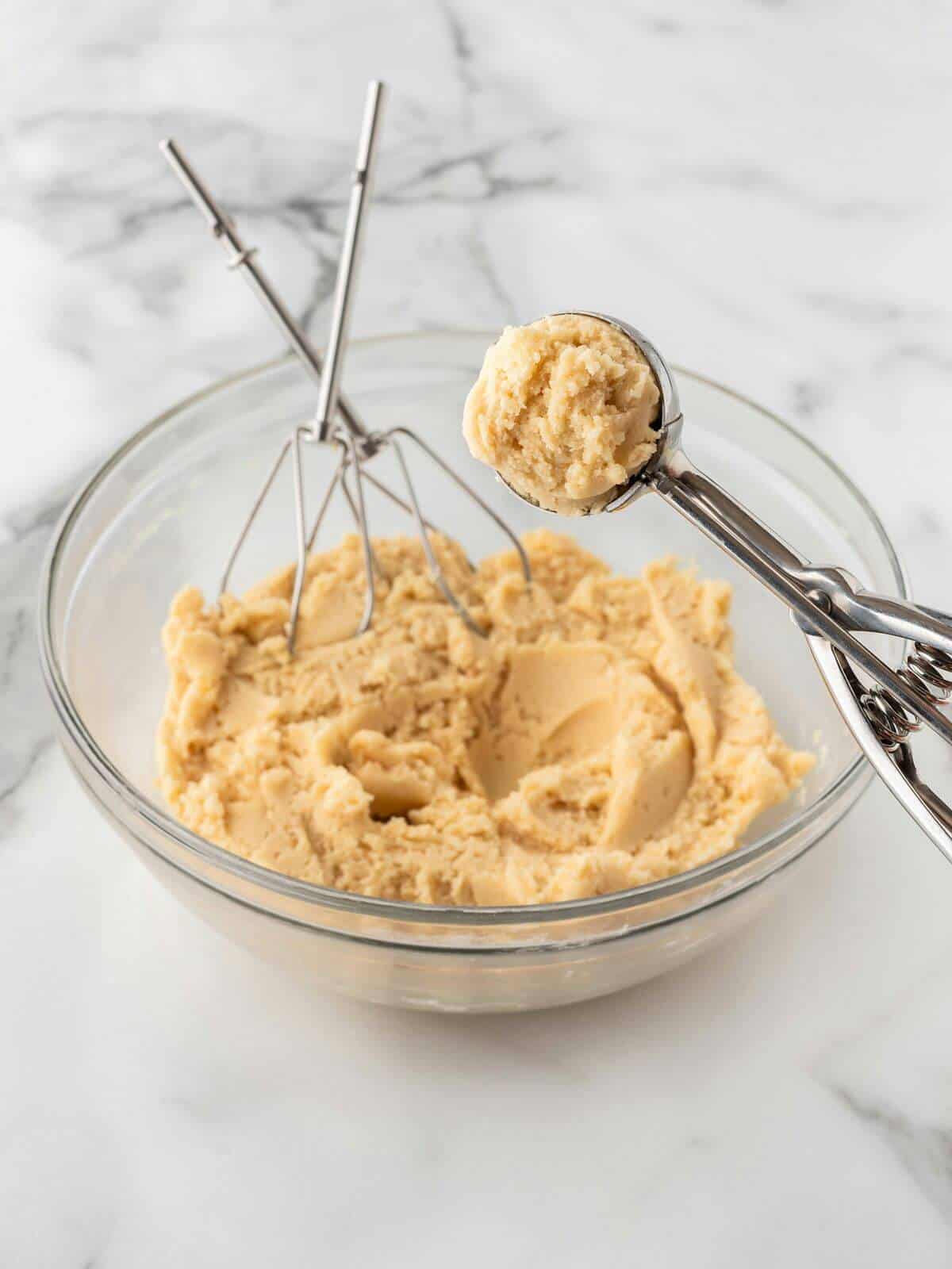 raw sugar cookie dough in glass mixing bowl with cookie scoop