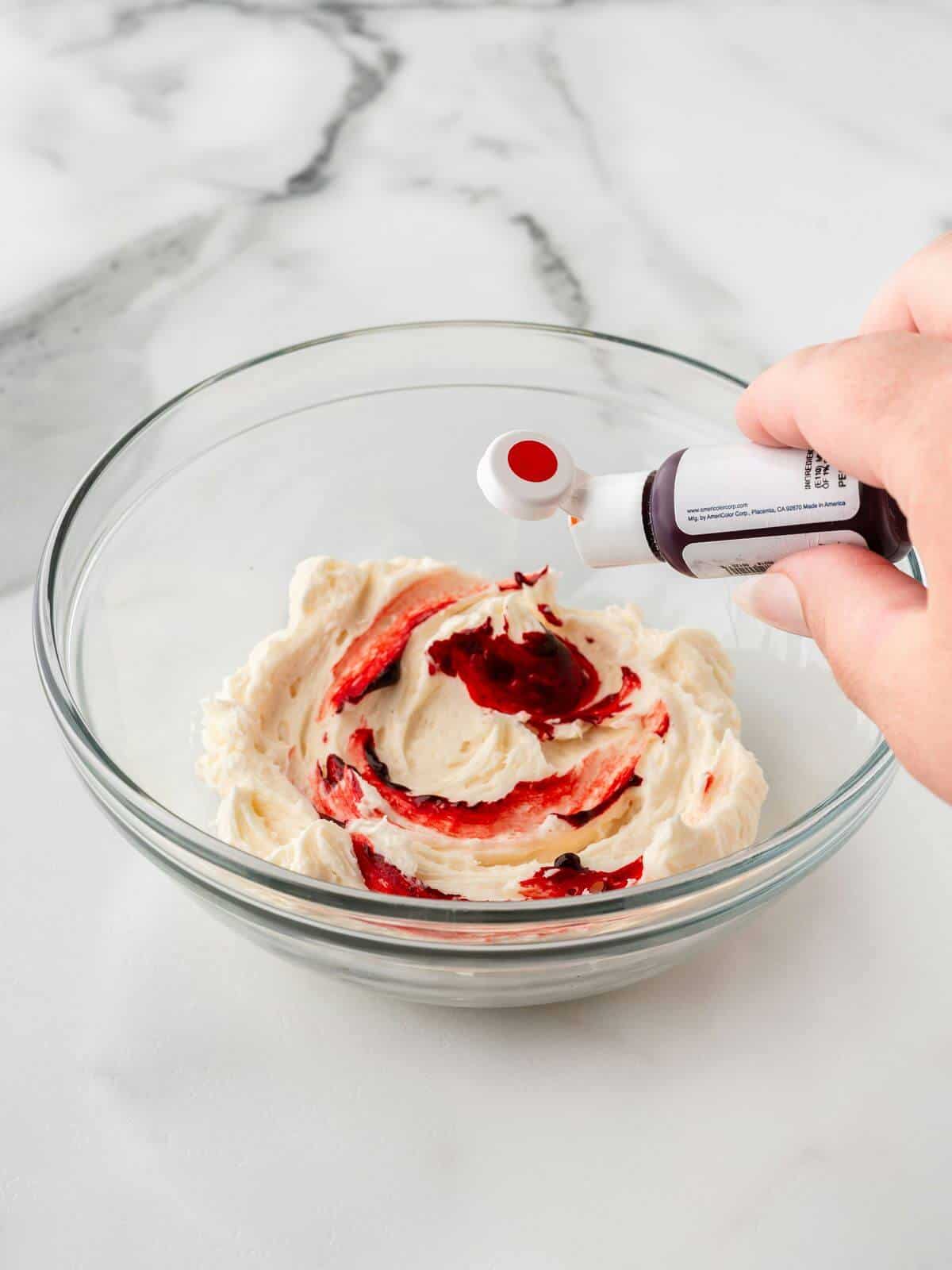 adding red food dye to white frosting in small glass bowl