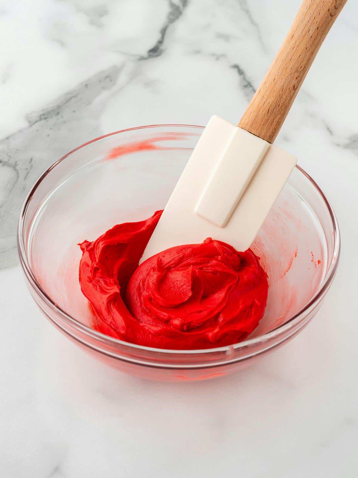 bowl of red icing being mixed with rubber spatula