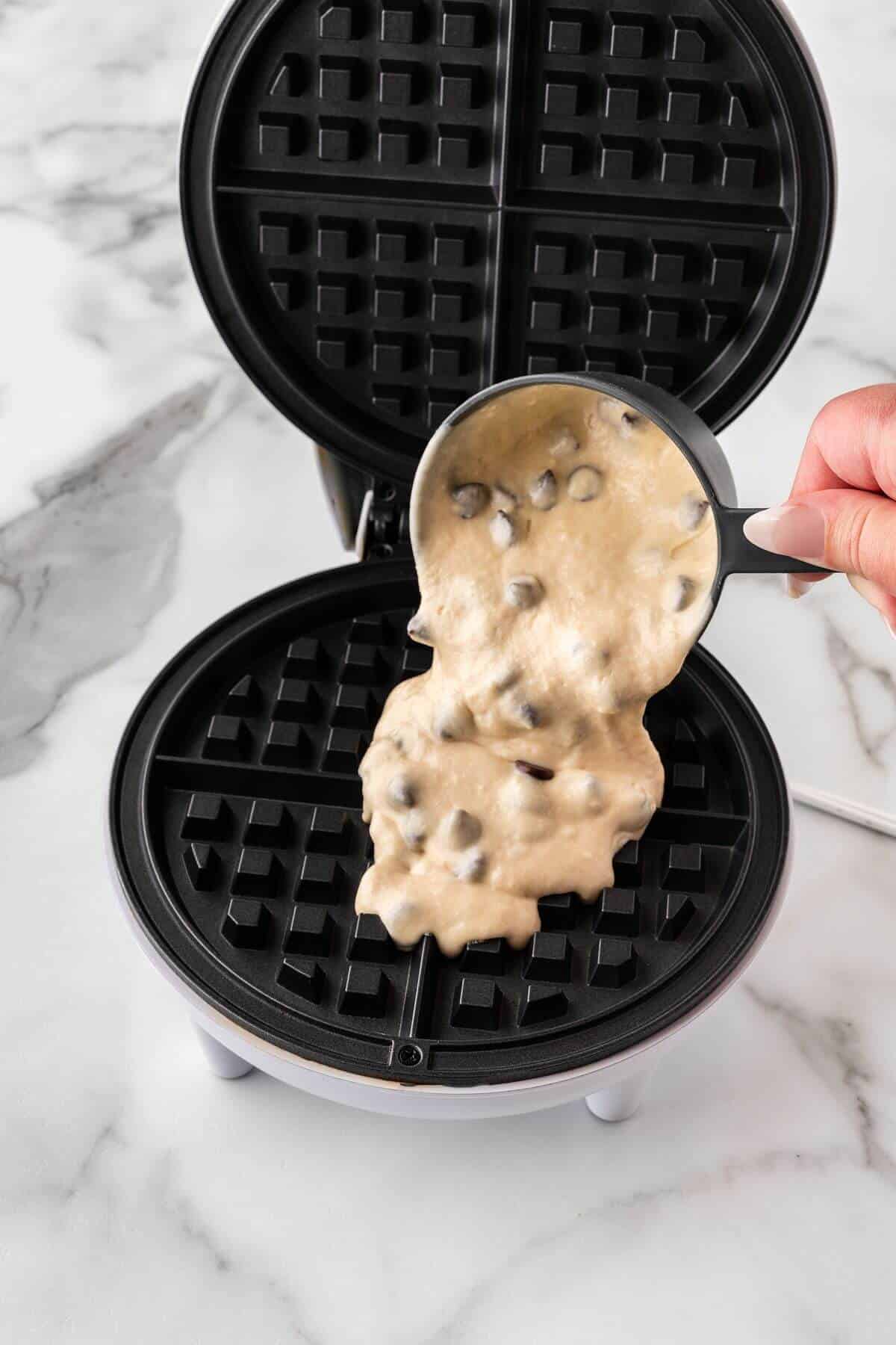 Pouring chocolate chip waffle batter in waffle iron.