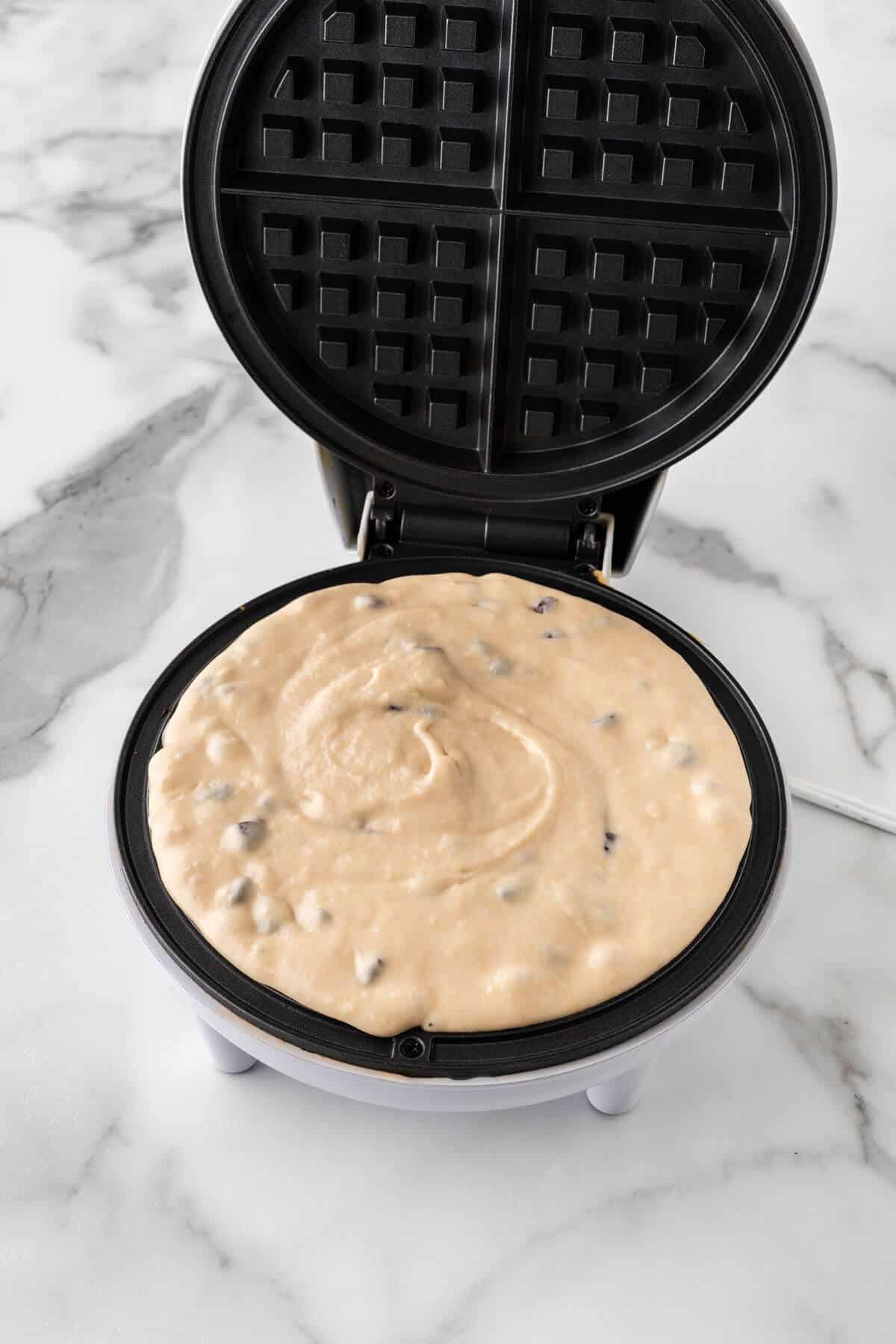 Chocolate chip waffle batter in waffle iron.