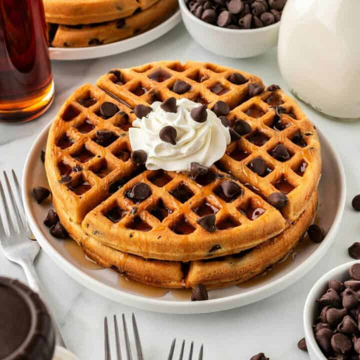 Stack of chocolate chip waffles with whipped cream and extra chocolate chips on top.