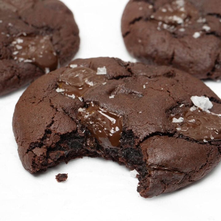 Upclose of dark chocolate chip cookie with bite taken out on parchment-lined baking sheet.