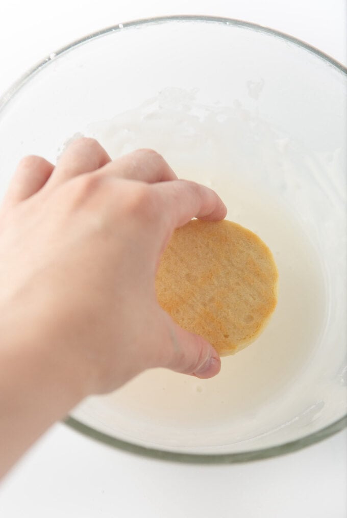 hand dipping top of sugar cookie into white icing