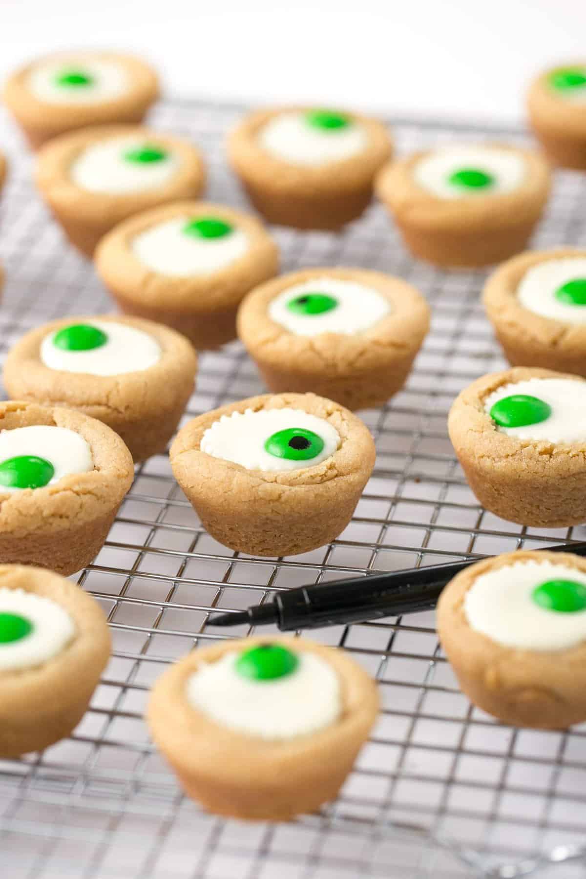 Mini white peanut butter cup cookies on wire cooling rack with black food pen. 