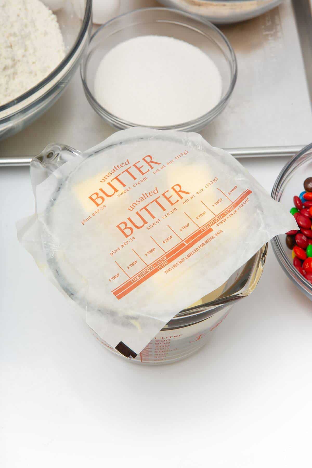 Butter wrappers on top of butter in glass measuring bowl to prevent splatter.