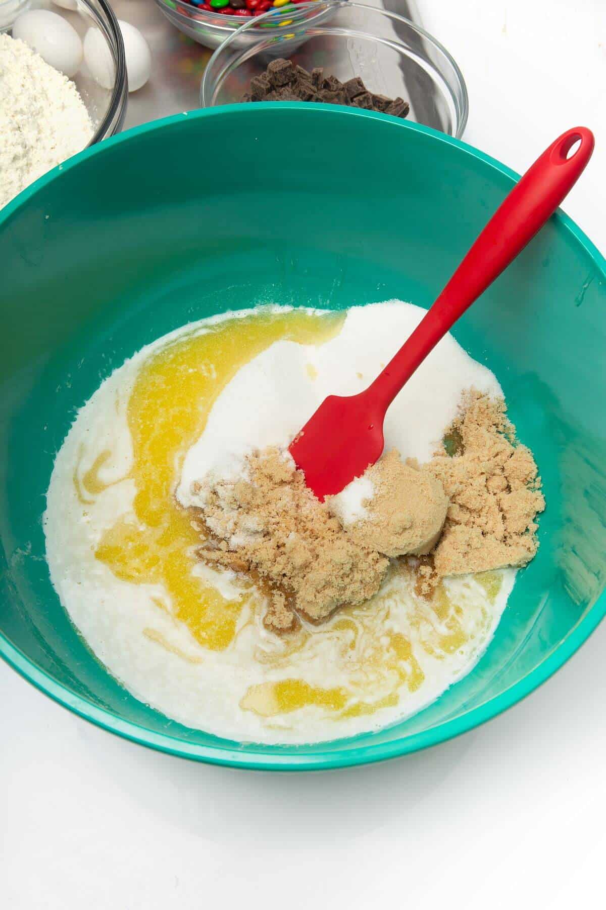 Sugars added to ingredients for freezer cookie down in mixing bowl with red spatula.