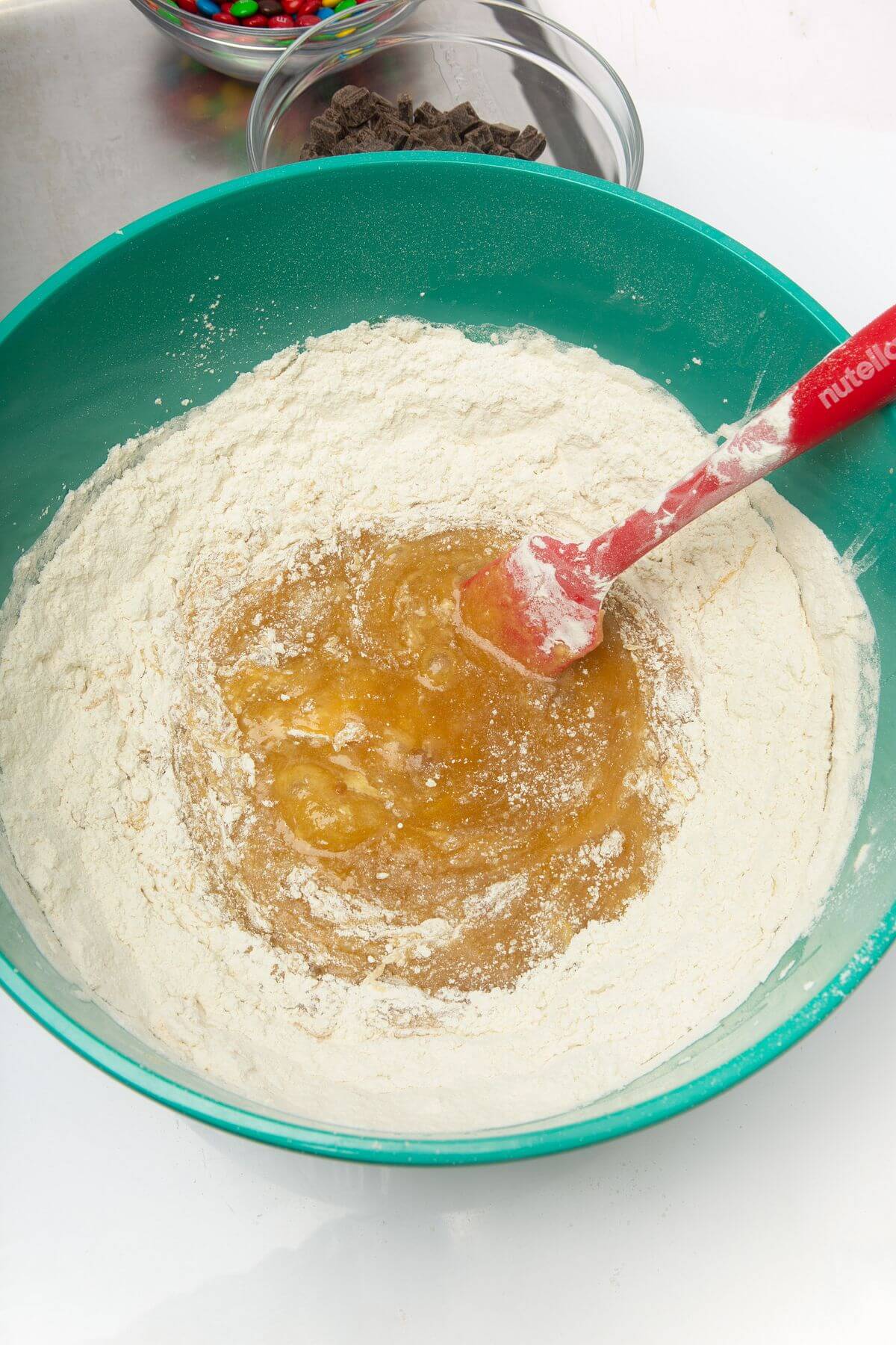 Flour added to ingredients in mixing bowl with spatula for freezer cookie dough.