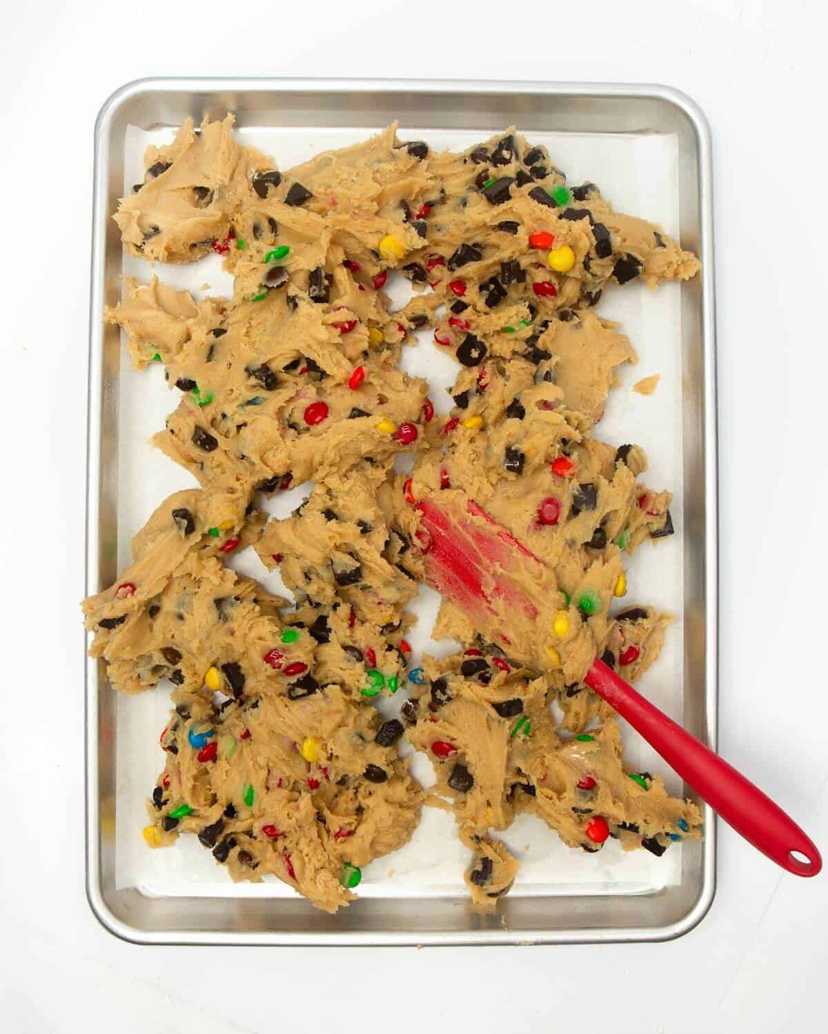 Spreading cookie dough onto metal pan with spatula.
