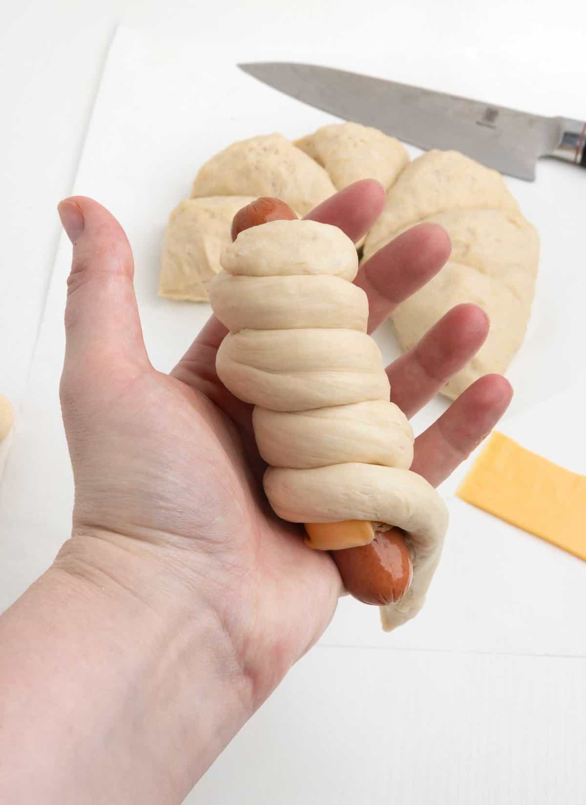 hand holding hot dog wrapped in pretzel dough