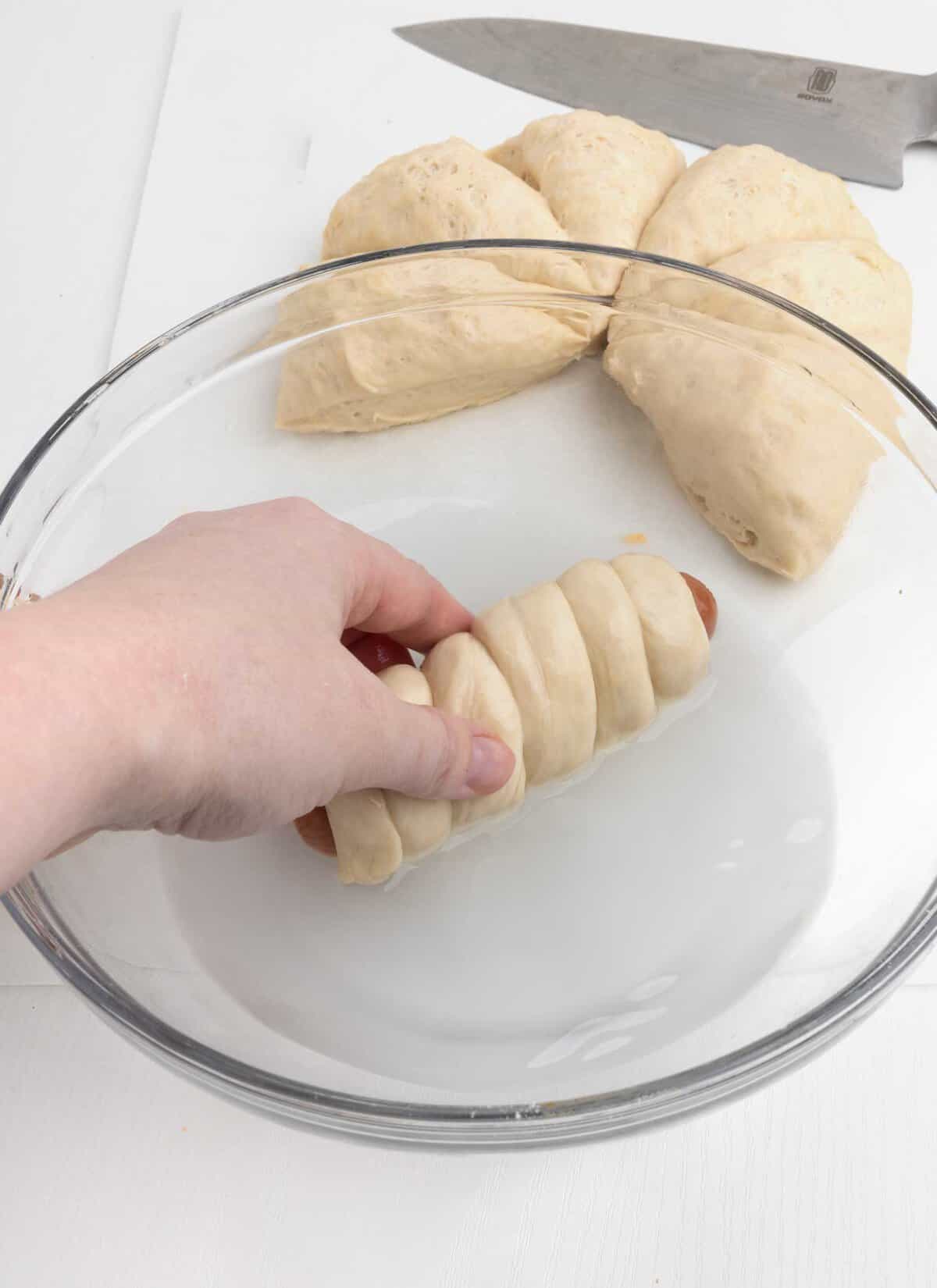 hand dipping pretzel hot dog in baking soda water bath