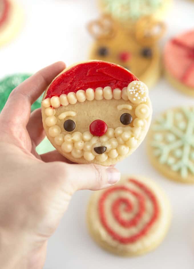 hand holding circle santa face sugar cookies decorated with M&M candy