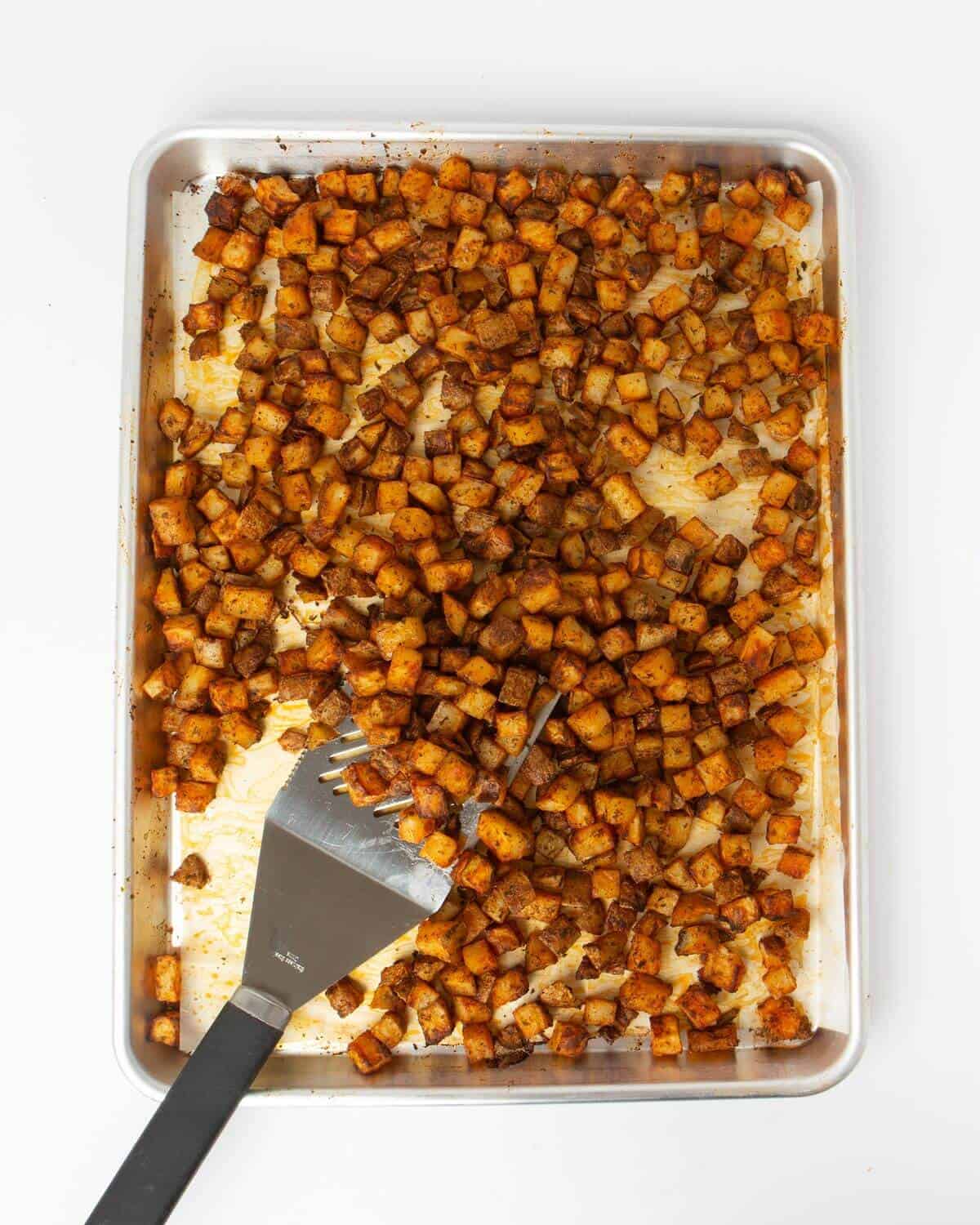 cooked breakfast potatoes on sheet pan lined with parchment paper and metal spatula