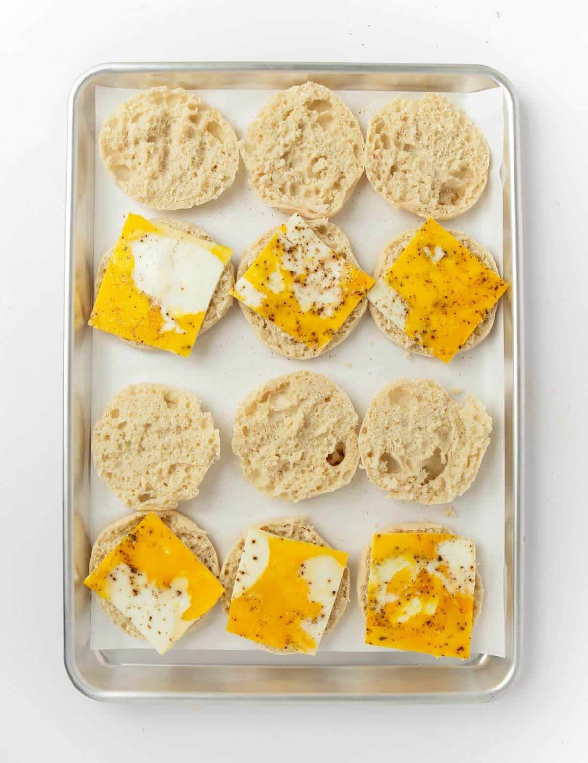opened english muffins on baking sheet with sheet pan eggs on top of half
