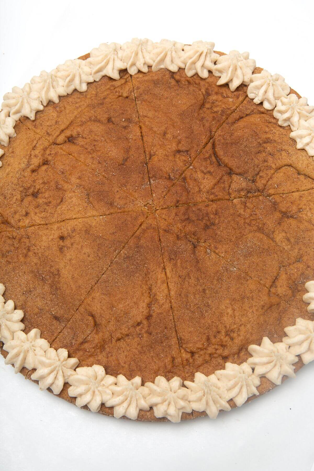 Baked snickerdoodle cookie cake with frosting around edges.