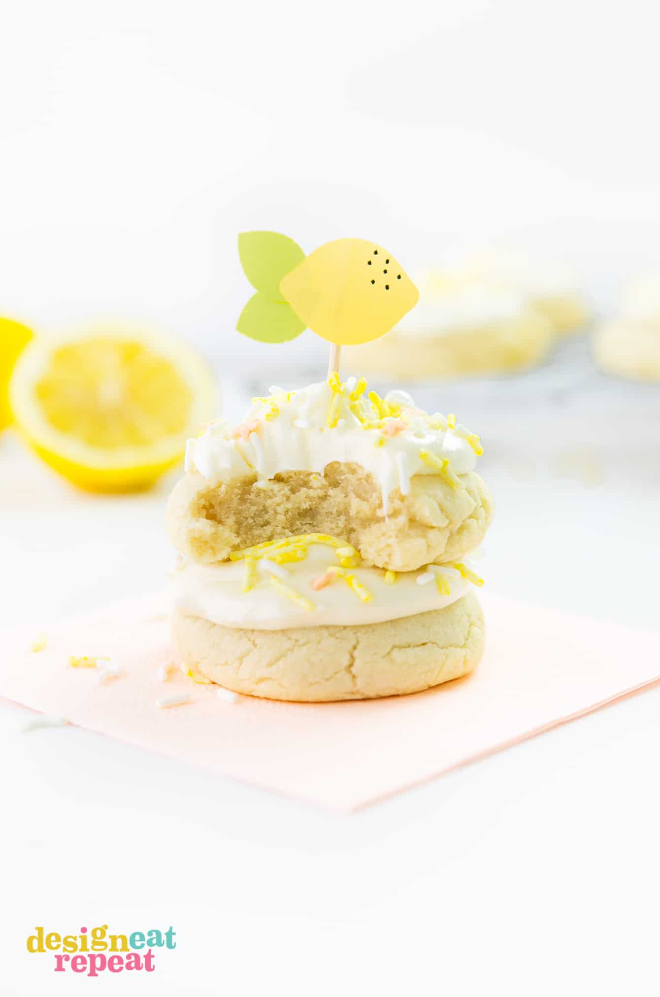 Welcome summertime with these delicious Soft & Thick Lemon Sugar Cookies. They are easy to make and are infused with a refreshing, light lemon flavor! Get the recipe at DesignEatRepeat.com Stack of thick lemon sugar cookies with frosting, yellow sprinkles, and paper lemon toothpick topper on top.