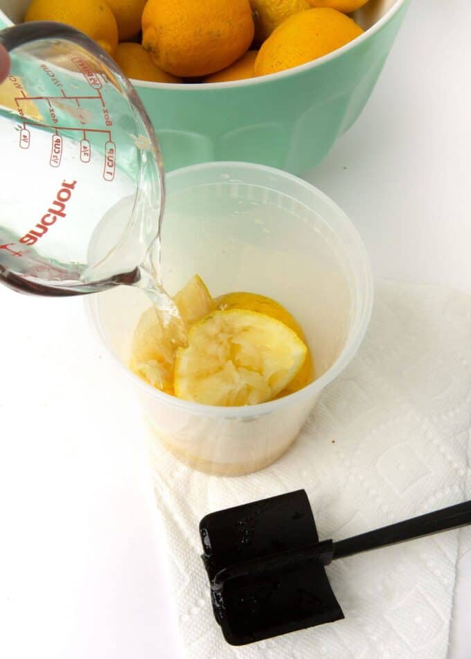 water pouring on top of lemon slices in plastic container with muddler